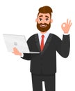 Happy bearded business man holding/showing a latest new laptop and gesturing/making okay or OK sign with hand fingers.
