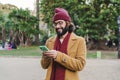 Happy bearded male hipster typing messages with a mobile phone social media app at city park outdoors. Portrait of young