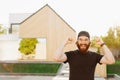 A happy bearded man with both hands up is being joyful near his new house