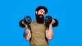 Happy bearded man with dumbbells up in hands. Athletic muscular man lifting dumbbells in sport club. Strong sportsman Royalty Free Stock Photo