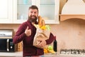 Happy bearded man holding a paper bag with food. Man with bag of groceries at modern kitchen. Delivery food, products to home Royalty Free Stock Photo