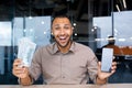 Happy bearded man in office holding stack of dollars and showing phone screen to camera, happy with winning, online Royalty Free Stock Photo