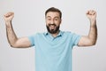 Happy bearded man raising his hands showing victory gesture near white wall. Handsome guy just won in a table game he Royalty Free Stock Photo