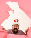 Happy bearded man in Santa hat looking through paper hole. Smiling guy in checkered shirt making hole in paper. Winter