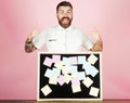 Happy bearded man standing at table with sticky notes on blackboard shows thumbs up. Notes, reminder. Royalty Free Stock Photo