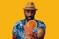 happy bearded mid adult african american man wearing Hawaiian shirt and hat smiling offering orange juice cocktail at