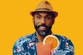 happy bearded mid adult african american man wearing Hawaiian shirt and hat smiling offering orange juice cocktail at