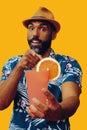 happy bearded mid adult african american man wearing Hawaiian shirt and hat smiling offering orange juice cocktail at