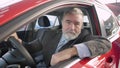 Happy bearded senior man showing thumb up and smiling at camera sitting on driver's seat in pricey new automobile in