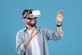 Happy bearded young man using VR headset to explore augmented reality on blue studio background Royalty Free Stock Photo
