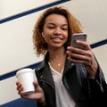 A happy beautiful African American girl with a white wireless earpiece in her ear is looking into the phone while sitting in the w Royalty Free Stock Photo