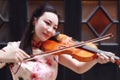 Happy beautiful Asian Chinese woman artist in traditional chi-pao cheongsam play violin in a garden close-up Royalty Free Stock Photo