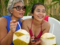 Happy and beautiful Asian Indonesian teenager girl using mobile phone enjoying Summer holidays drinking coconut at tropical resort Royalty Free Stock Photo