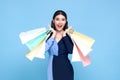 Happy beautiful Asian shopaholic women wearing blue dress and holding shopping bags isolated on blue background