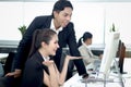 Happy beautiful Asian woman officer talking and collaborating with colleague coworker team while working on desktop computer at Royalty Free Stock Photo