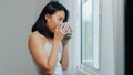 Happy beautiful Asian woman smiling and drinking a cup of coffee or tea near the window in bedroom. Royalty Free Stock Photo