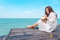 A happy beautiful asian woman on white dress sitting at the wooden terrace and drinking coconut juice with sea Royalty Free Stock Photo