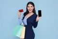 Happy beautiful asian women showing credit card and smartphone and holding shopping bags isolated on blue background Royalty Free Stock Photo