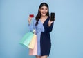 Happy beautiful asian women showing credit card and smartphone holding shopping bags isolated on blue background Royalty Free Stock Photo