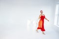 Happy beautiful bald woman with red hair meloman in long red dress raising arms