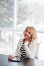 Happy beautiful blonde woman with tablet sitting at table in co-working space, looking at camera and smiling. Medium shot. Royalty Free Stock Photo