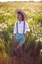 Happy a beautiful boy child in a hat stands on a field with white dandelions at sunset in summer. Royalty Free Stock Photo