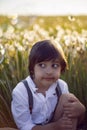 Happy a beautiful boy child sit on a field with white dandelions at sunset in summer. Royalty Free Stock Photo