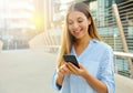 Happy beautiful business woman typing on her smart phone while standing in modern city street. Copy space Royalty Free Stock Photo