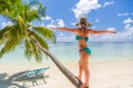 Woman in hot sunny weather standing on a palm tree and enjoying tropical beach vacation, carefree holiday Royalty Free Stock Photo