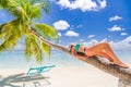 Woman in hot sunny weather laying down on a palm tree and enjoying tropical beach vacation, carefree holiday Royalty Free Stock Photo