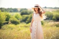 Happy beautiful girl stands in field in summer while wearing a sunhat and midi dress. Lifestyle