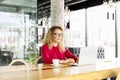 Happy beautiful curly hair blonde young female at coffee shop using laptop, smiling. Young attractive woman freelancer wearing gla Royalty Free Stock Photo