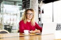 Happy beautiful curly hair blonde young female at coffee shop using laptop, smiling. Young attractive woman freelancer wearing gla Royalty Free Stock Photo