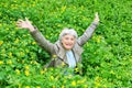 Happy beautiful elderly woman sitting arms outstretched on a glade of yellow flowers in spring. Royalty Free Stock Photo