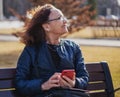 Happy beautiful elderly woman sitting with a smartphone on a bench on a spring sunny day Royalty Free Stock Photo