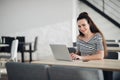 Happy beautiful freelance working woman sitting in a cafe with modern interior and typing something in her laptop Royalty Free Stock Photo