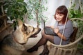 happy beautiful girl in chair using her laptop with cute big dog. Adult middle aged woman with shepherd. Friendship and Royalty Free Stock Photo