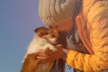 Happy beautiful girl owner in woolen hat and jacket with scarf hugging her little chihuahua pet dog with love and care on blue sky Royalty Free Stock Photo