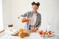 Happy beautiful girl pouring grapefruit detox smoothie in glass smiling over white wall. Healthy diet nutrition.