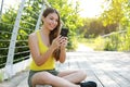 Happy beautiful girl sitting on the floor and writing message on smartphone in the park Royalty Free Stock Photo