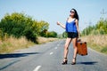 Happy beautiful girl traveler with a suitcase on the road, hitch Royalty Free Stock Photo