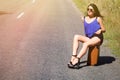 Happy beautiful girl traveler with a suitcase on the road, hitch Royalty Free Stock Photo