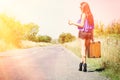 Happy beautiful girl traveler with a suitcase on the road, hitchhiking. The concept of travel, adventure, vacation, freedom. Royalty Free Stock Photo