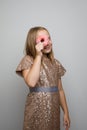 Happy beautiful kid girl in gold dress standing with pink glazed donut, studio portrait. Holiday birthday party concept