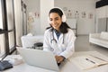 Happy beautiful Latin doctor woman working at laptop