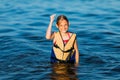 Happy beautiful little girl in a life jacket, swimming in the sea and showing a winning gesture. Summer holiday, vacation