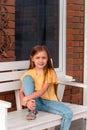 happy beautiful little girl with long blonde hair wearing casual clothes sitting on a bench Royalty Free Stock Photo