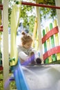 Happy beautiful little redhead girl climbs the slide on the playground