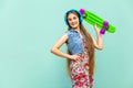 The happy beautiful long haired blonde girl in dress and blue headphones, having fun with green plastic penny skate.