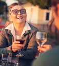 Happy beautiful mature woman in glasses 60 years old sitting in a cafe with her girlfriend drinking wine in a street cafe Royalty Free Stock Photo